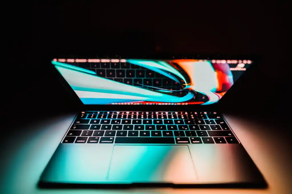 Open laptop showing a bright, colorful abstract wallpaper reflected on the keyboard in a dark setting.